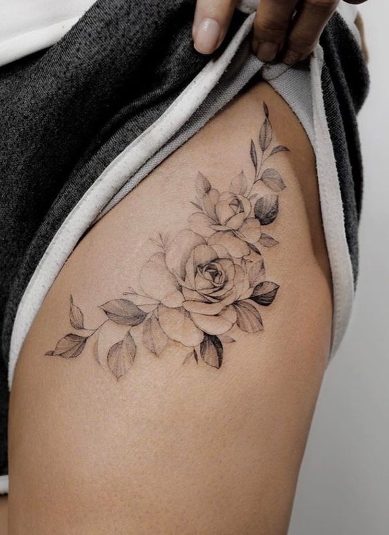 Delicate floral tattoo on thigh with roses and leaves, showcasing intricate black and grey detailing.