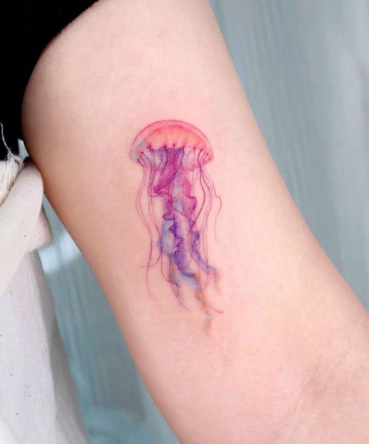 Watercolor jellyfish tattoo on arm, showcasing vibrant pink and purple hues with delicate tentacles.