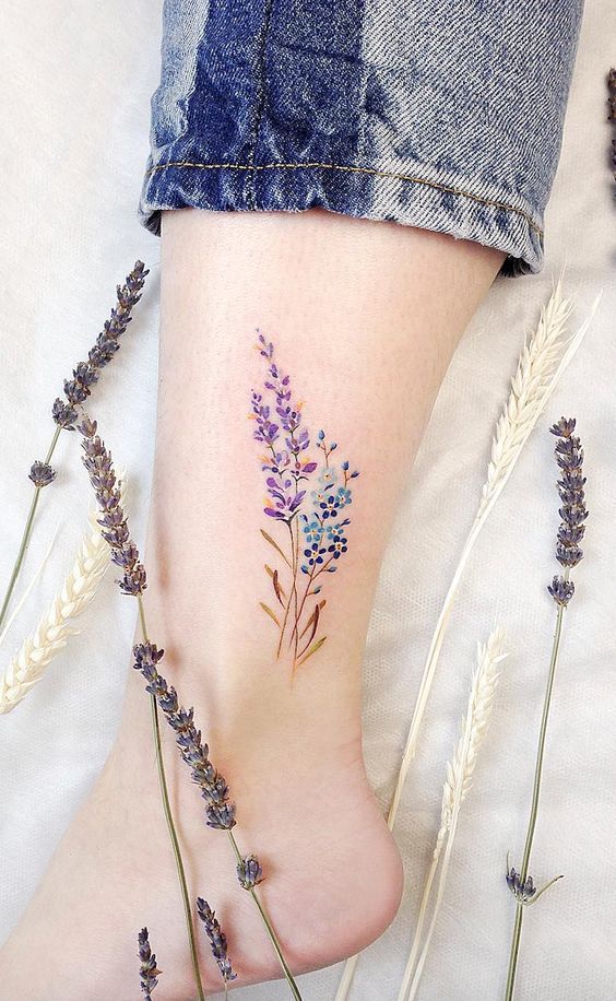 Delicate lavender tattoo on ankle surrounded by lavender flowers and denim jeans.