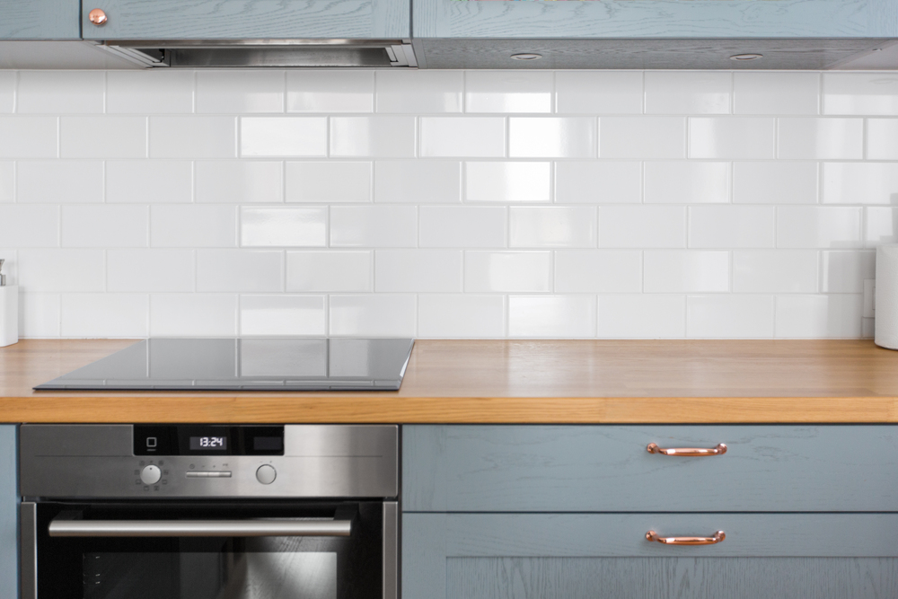 Modern kitchen with blue cabinets, wooden countertop, stainless steel oven, and white subway tile backsplash.