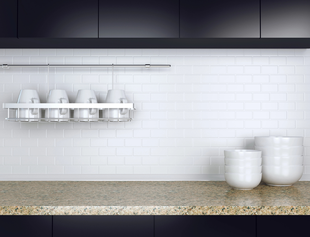 Minimalist kitchen with white cups and bowls against a sleek subway tile backsplash and granite countertop.