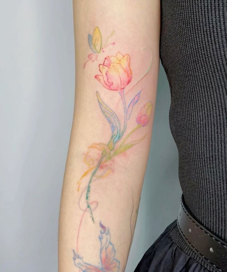 Colorful floral tattoo with abstract butterflies on arm, showcasing delicate, pastel hues.