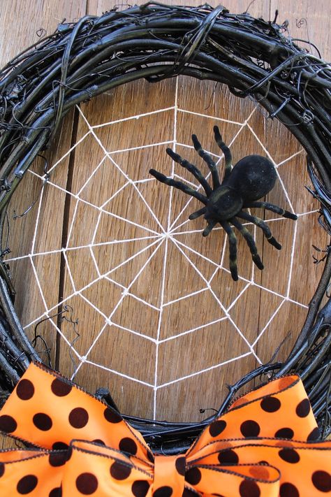 Halloween wreath with spider and web on wood background, featuring an orange polka dot bow.