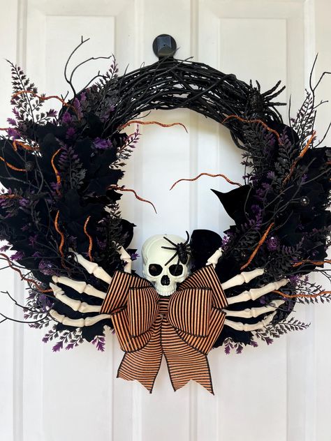 Spooky Halloween wreath with skeleton hands, black foliage, and orange bow on a white door.