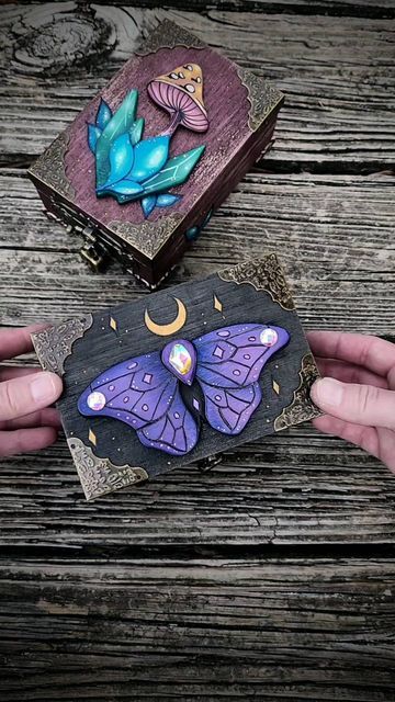 Handcrafted mystical box with colorful crystals and a purple moth design, held by hands on a wooden surface.