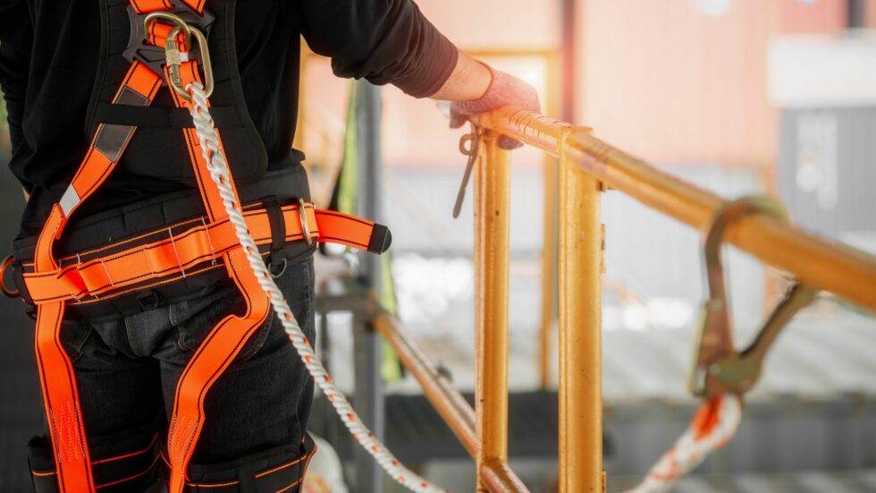 Worker wearing a safety harness while securing on a high platform with metal railing.