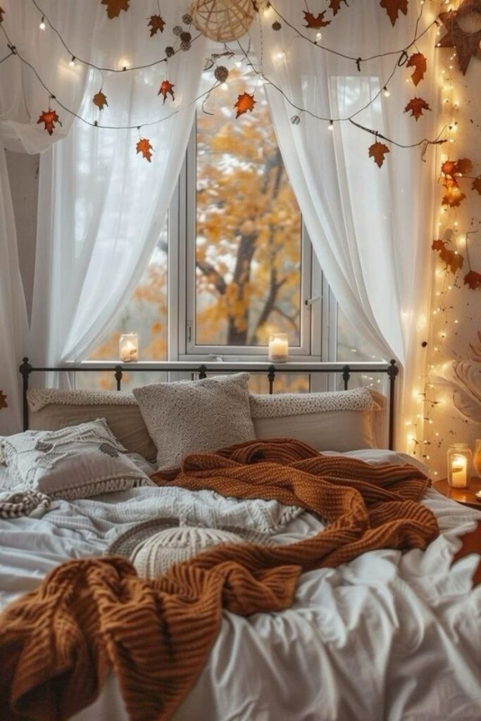 Cozy autumn bedroom with string lights, fall leaves, and warm blankets by a window overlooking vibrant orange foliage.