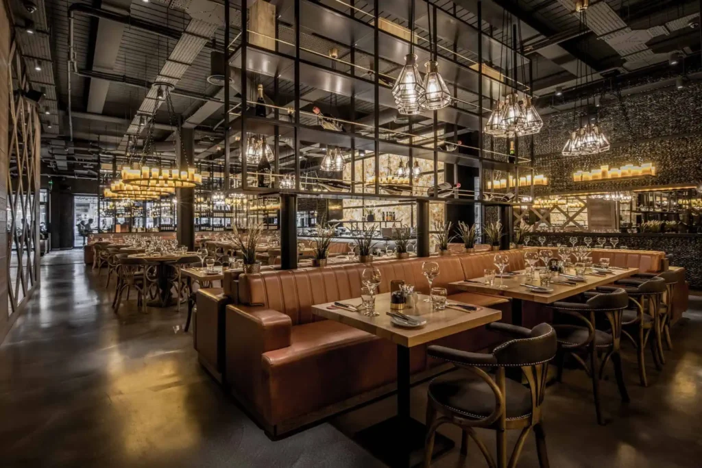 Modern restaurant interior with elegant lighting, brown leather seating, and set tables, creating a warm dining atmosphere.