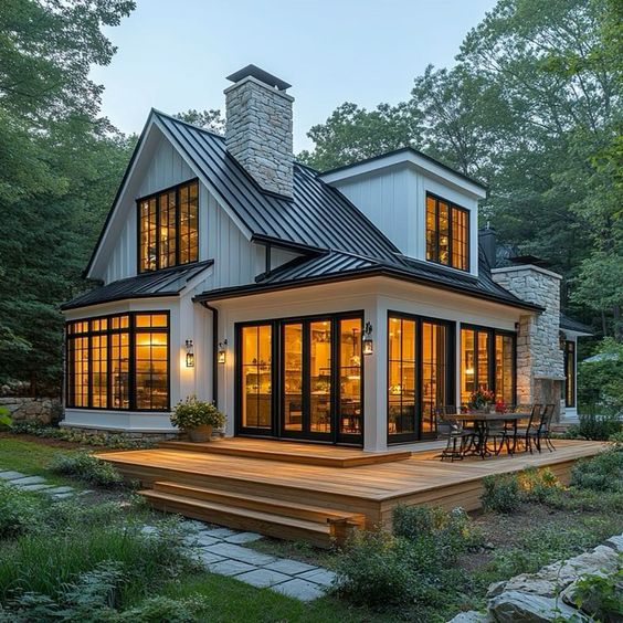 Cozy modern cottage with large windows, stone chimney, and wooden deck in a lush forest setting.