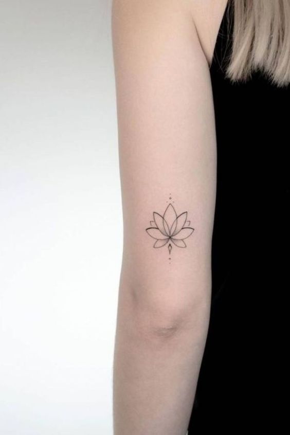 Minimalist lotus flower tattoo on upper arm against a light background.