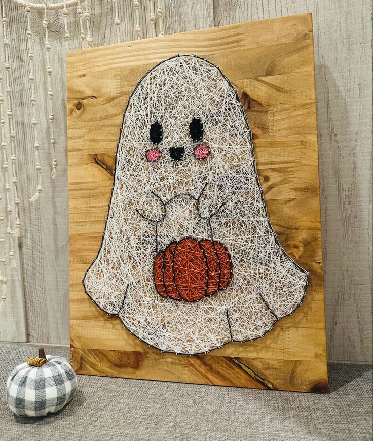 String art of a cute ghost holding a pumpkin on wooden background. Perfect Halloween decoration idea.