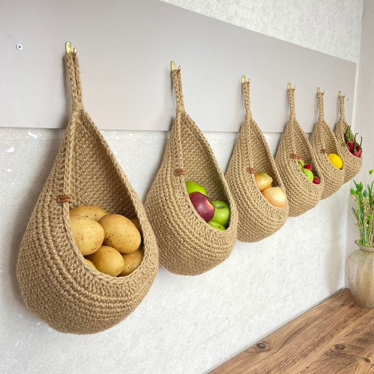 Hanging woven baskets filled with fresh vegetables and fruits, including potatoes, apples, onions, and peppers in a kitchen.