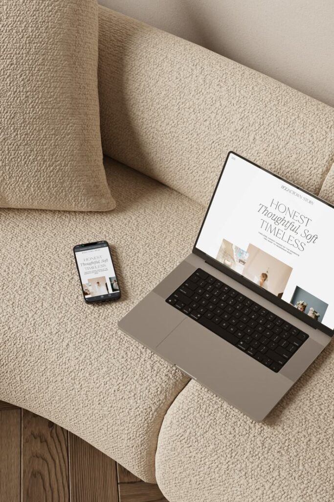 Laptop and smartphone displaying a minimalist website design on a beige sofa, emphasizing style and sophistication.