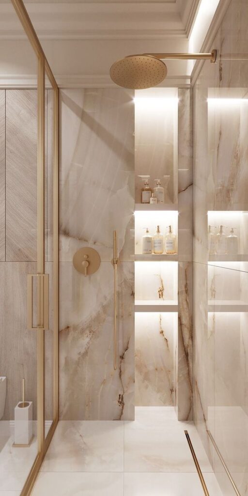 Luxurious marble shower with gold fixtures and illuminated shelves showcasing elegant toiletries.