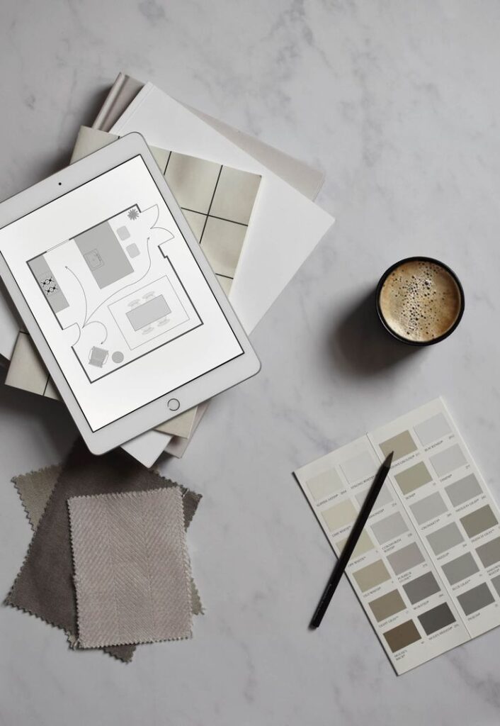 Tablet with interior design plan, fabric swatches, and color palette with coffee on marble surface.