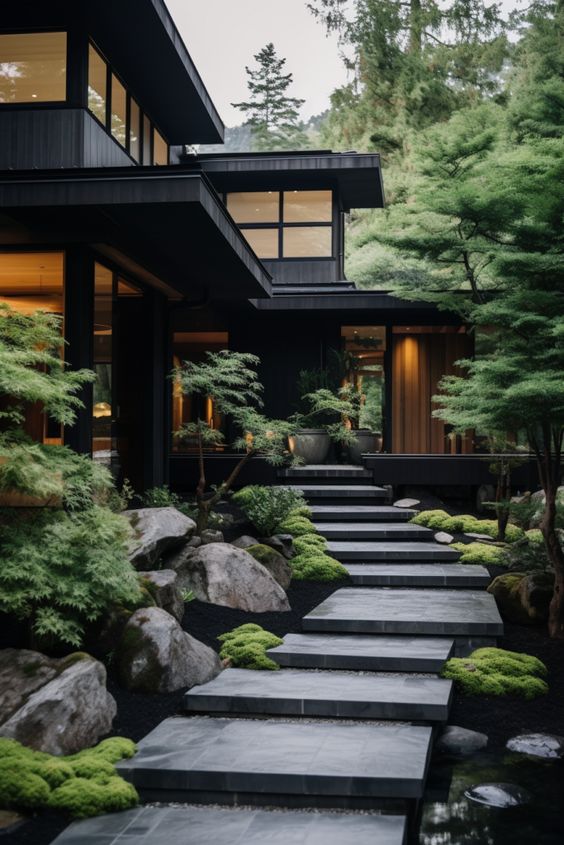 Modern home with large windows, surrounded by lush gardens and stone paths leading to the entrance.