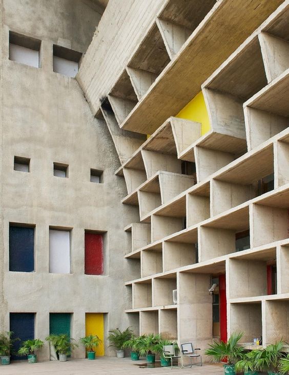 Modern architectural building with geometric concrete design and colorful accents, surrounded by green plants.