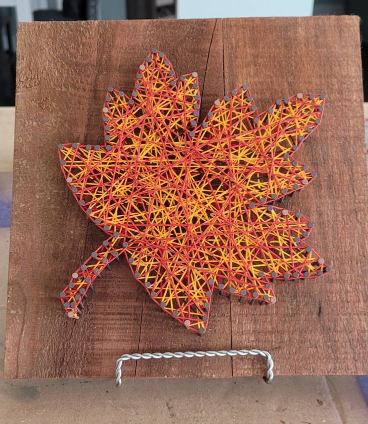 Maple leaf string art on wood, featuring intricate red and yellow thread designs for autumn decor.