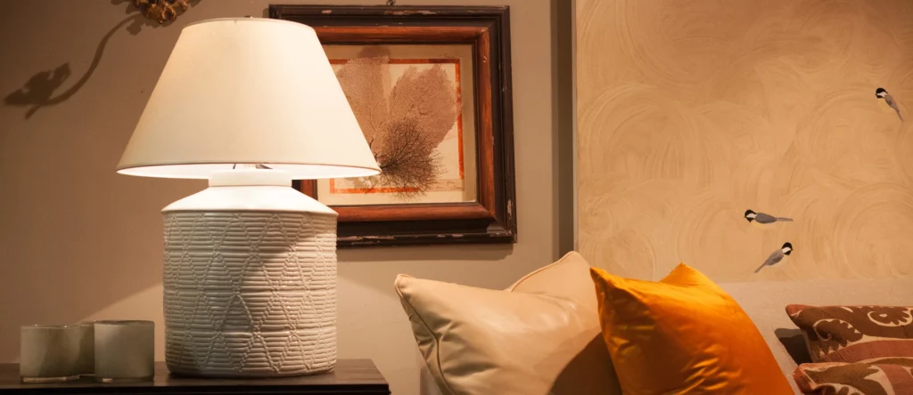 Cozy living room lamp with art, beige and orange pillows, and decorative wall accents. Warm, inviting ambiance.