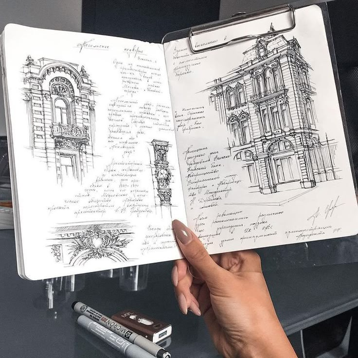 Architectural sketches and notes in a journal, held by a person, with art supplies on a table.