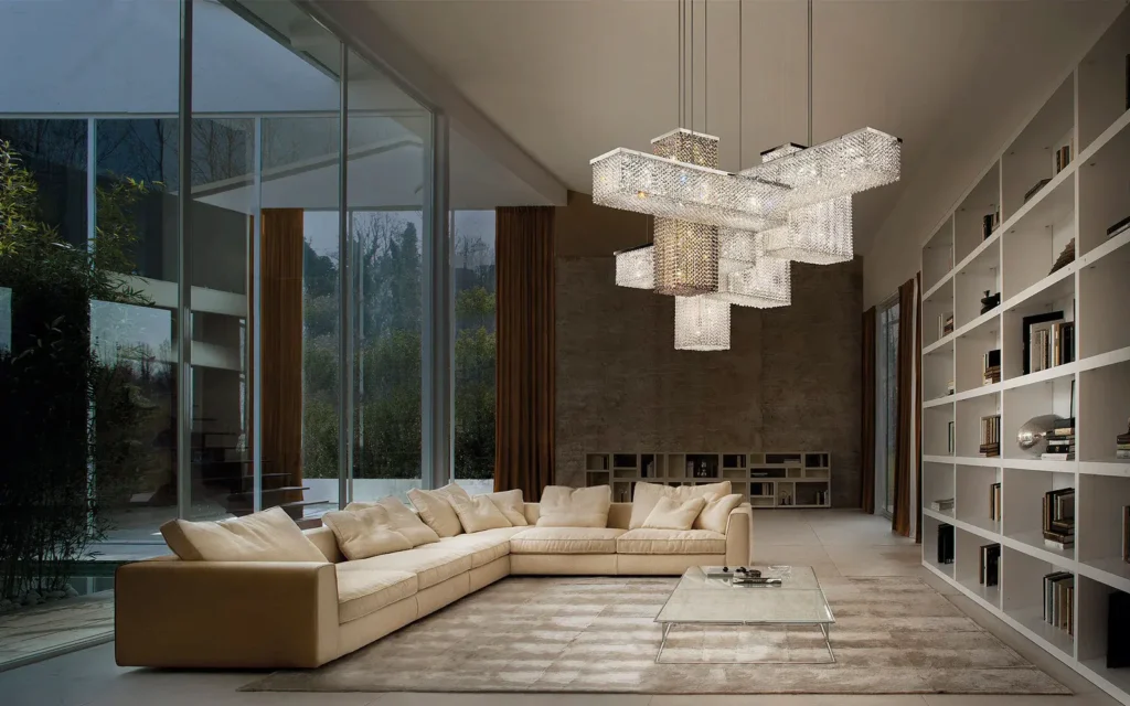 Modern living room with beige sectional sofa, geometric chandelier, and large windows overlooking a garden.