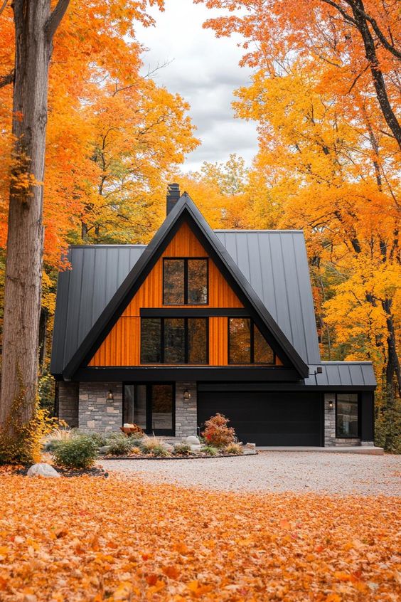 Modern A-frame house surrounded by vibrant autumn foliage and fallen leaves.