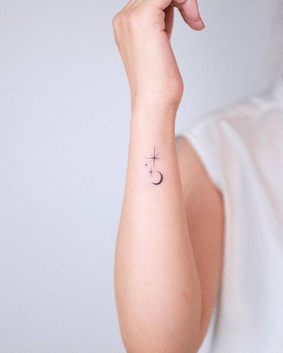 Minimalist moon and stars tattoo on forearm against a white background. Simple cosmic design.