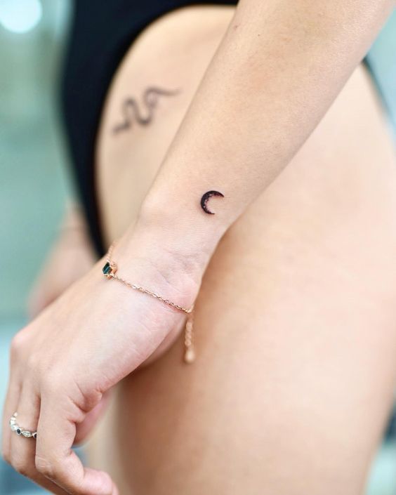 Minimalistic crescent moon and wave tattoos on forearm and hip, with a delicate bracelet.