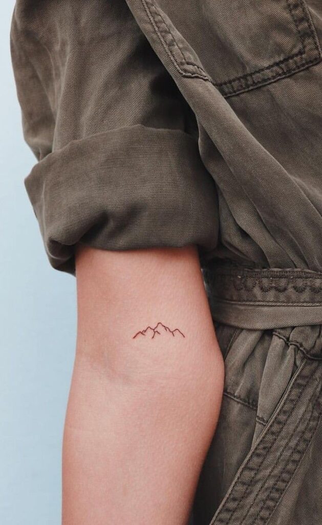 Minimal mountain tattoo on forearm in a brown jacket sleeve, close-up.