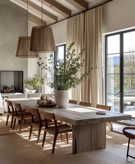 Modern dining room with a wooden table, chairs, rustic pendant lights, and a vase of greenery. Bright, natural lighting.