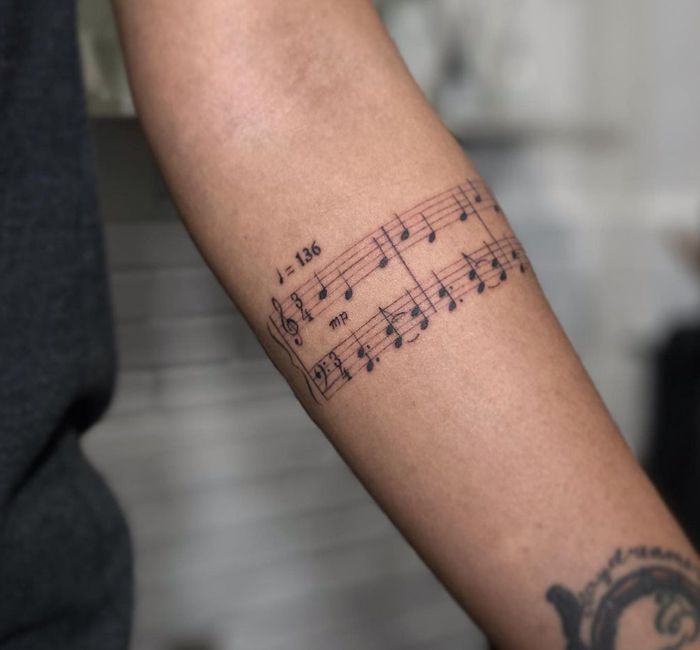 Tattoo of musical notes and tempo marking on a forearm, showcasing intricate music notation art.