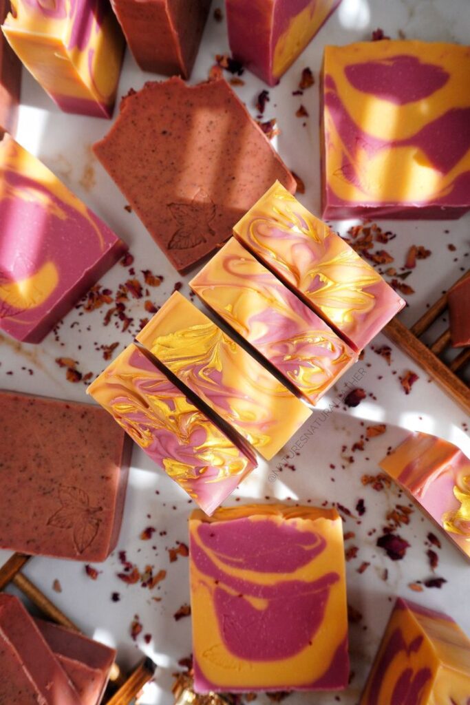 Colorful handmade swirl soap bars on a white background, surrounded by rose petals and cinnamon sticks.