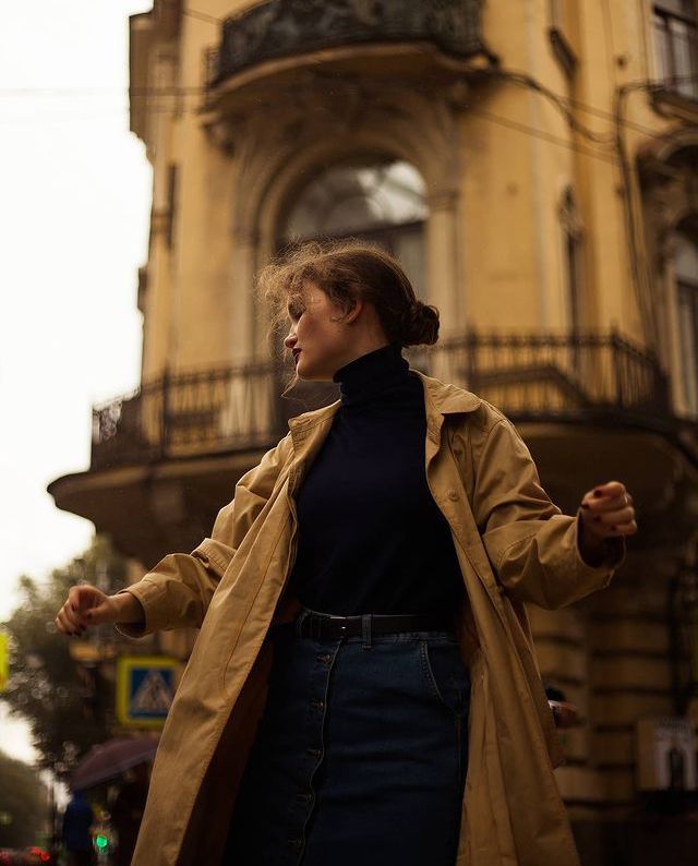 Woman in a trench coat stands in front of historic building, capturing an autumn street scene.