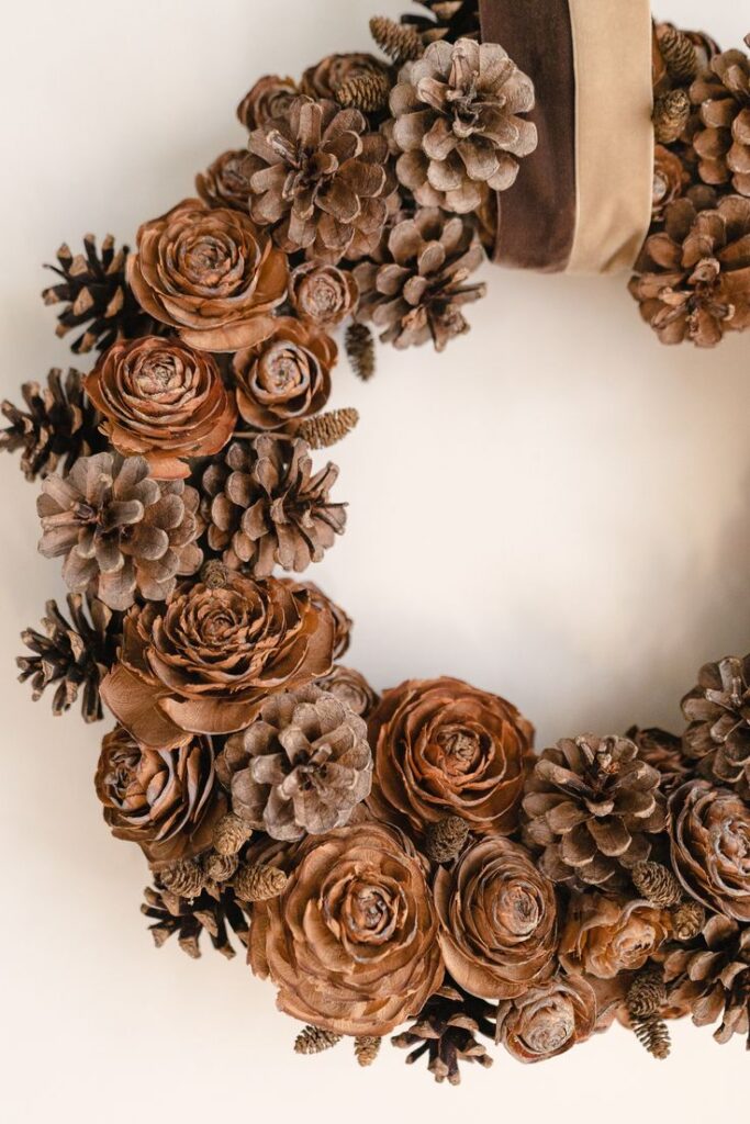 Rustic pinecone wreath with brown roses and ribbon, perfect for autumn or holiday home decor.