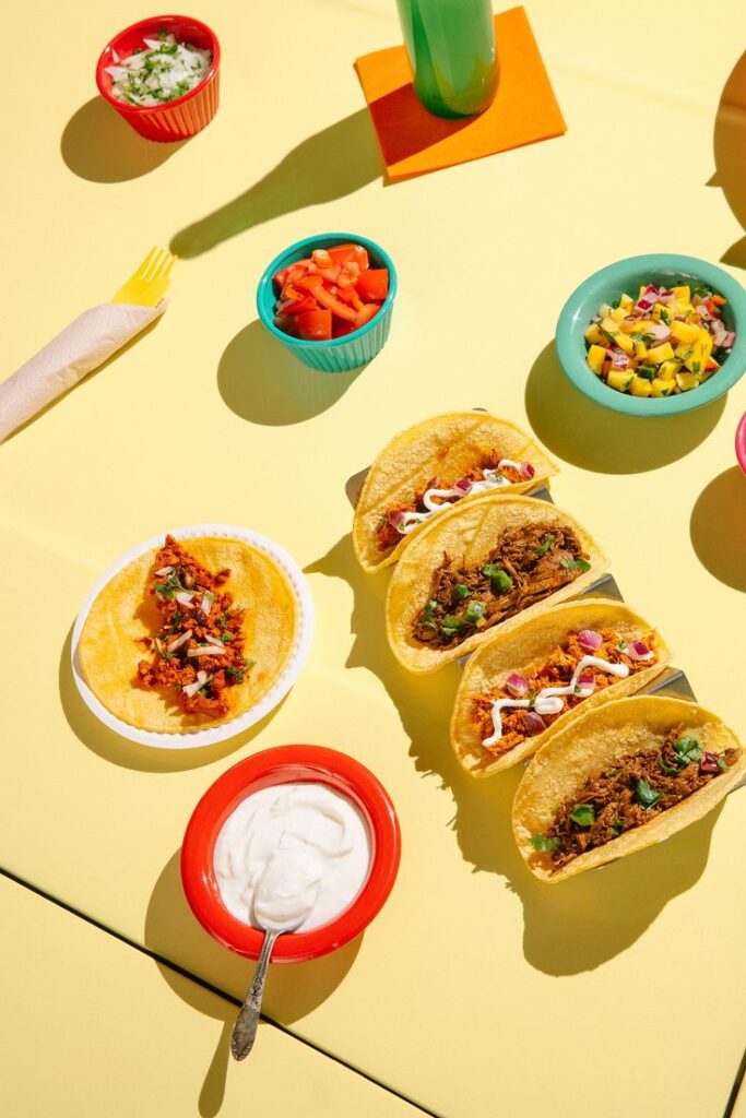 Colorful tacos with assorted toppings and sauces on a yellow table, ready for a delicious meal.