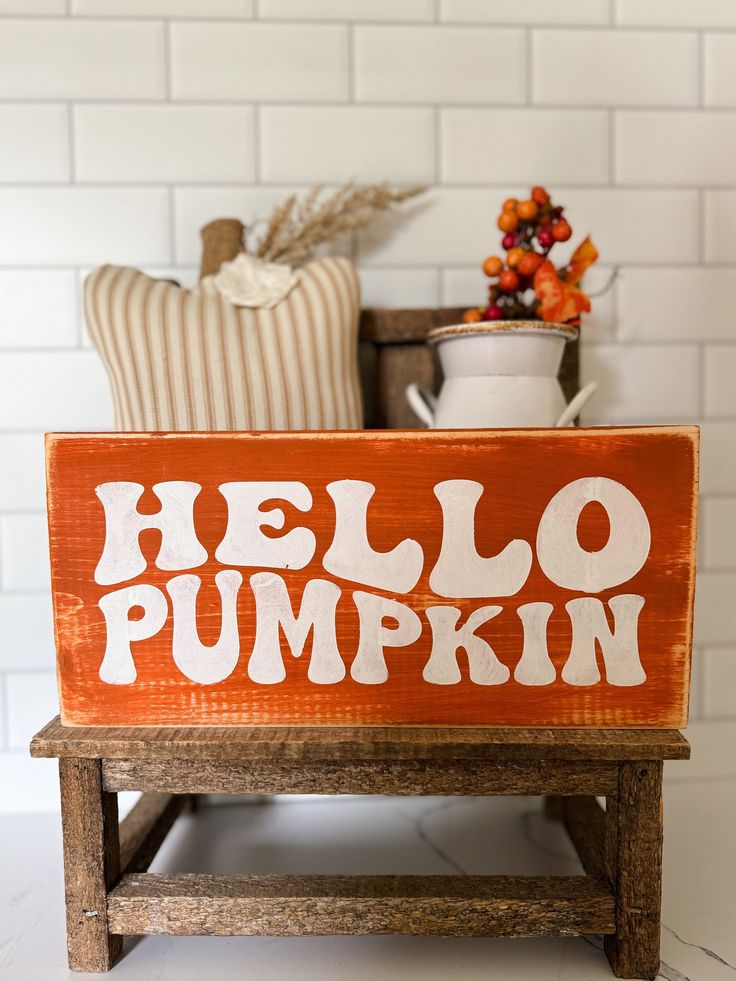 Orange Hello Pumpkin sign with autumn decor on rustic wooden table, white subway tile background. Cozy fall vibes.