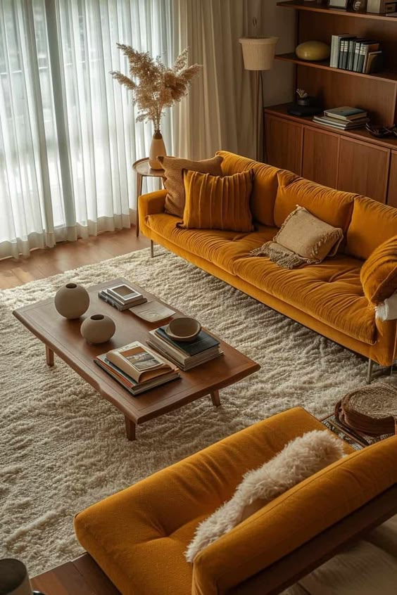 Cozy living room with mustard sofas, wooden table, and soft rug under natural light from sheer curtains.