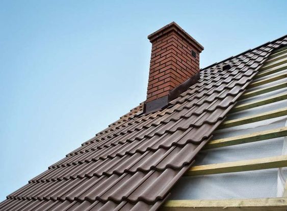 Brown tiled roof with a red brick chimney against a clear blue sky, showcasing durable roofing materials.