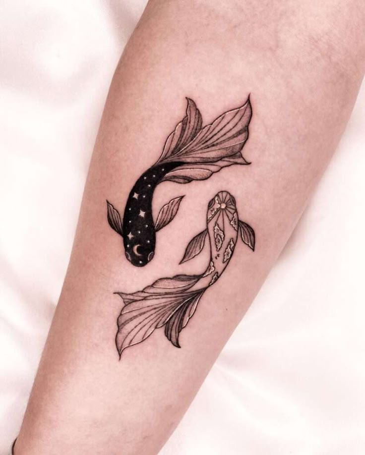 Tattoo of two koi fish on forearm, one dark with stars and one light with geometric patterns.