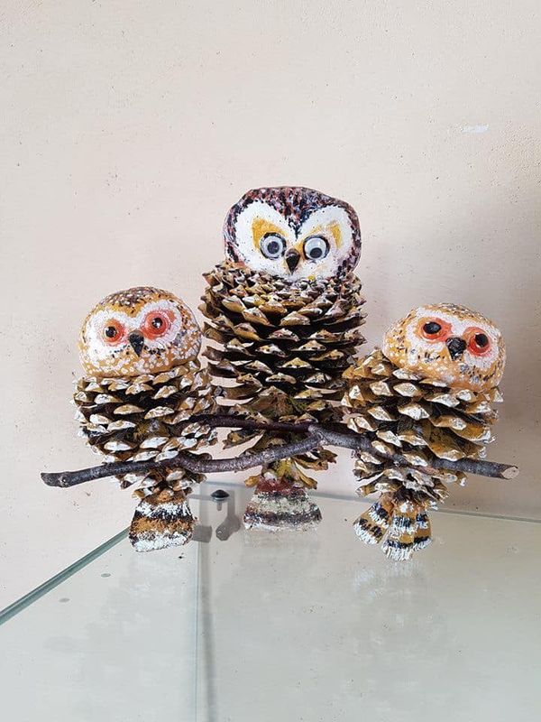 Three pinecone owls perched on a branch, crafted with natural materials for decorative purposes.