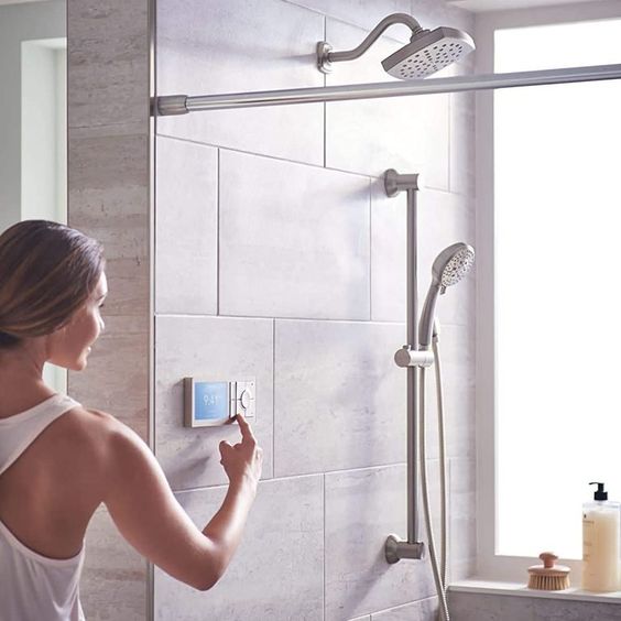 Woman adjusting smart shower control in modern bathroom.