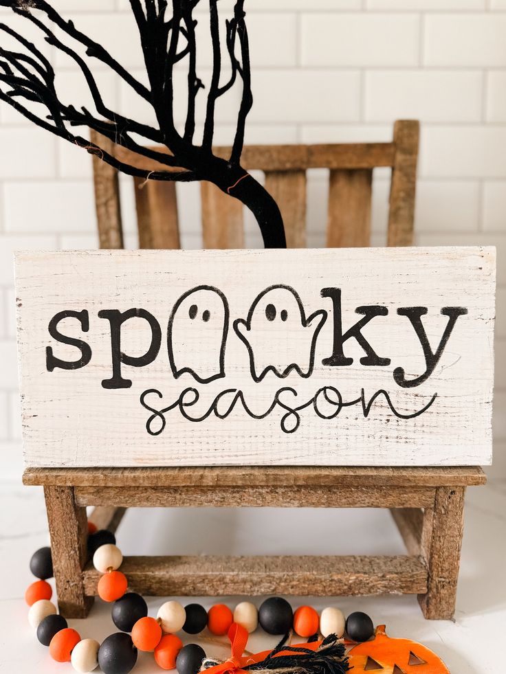 Rustic Halloween decor with spooky season sign, black tree, and colorful beads on wooden chair.