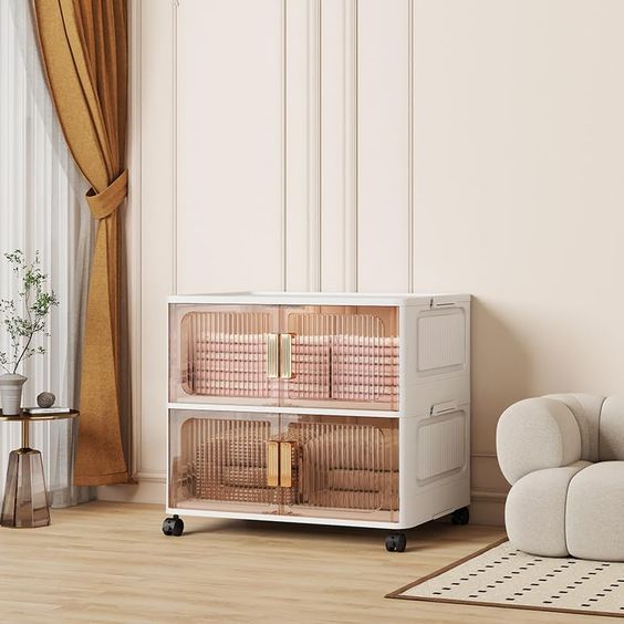 Modern storage cabinet with transparent doors in a stylish living room featuring a beige sofa, gold curtains, and white walls.