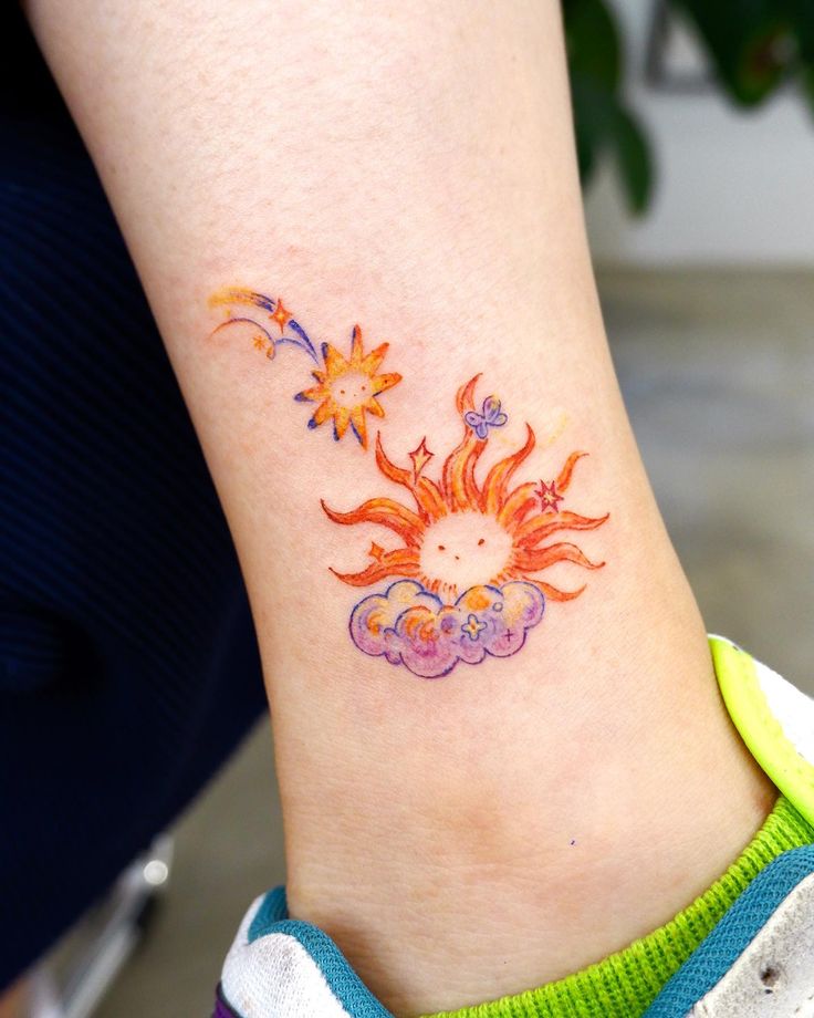 Colorful sun and cloud tattoo with stars and swirls on ankle, showcasing vibrant celestial design elements.