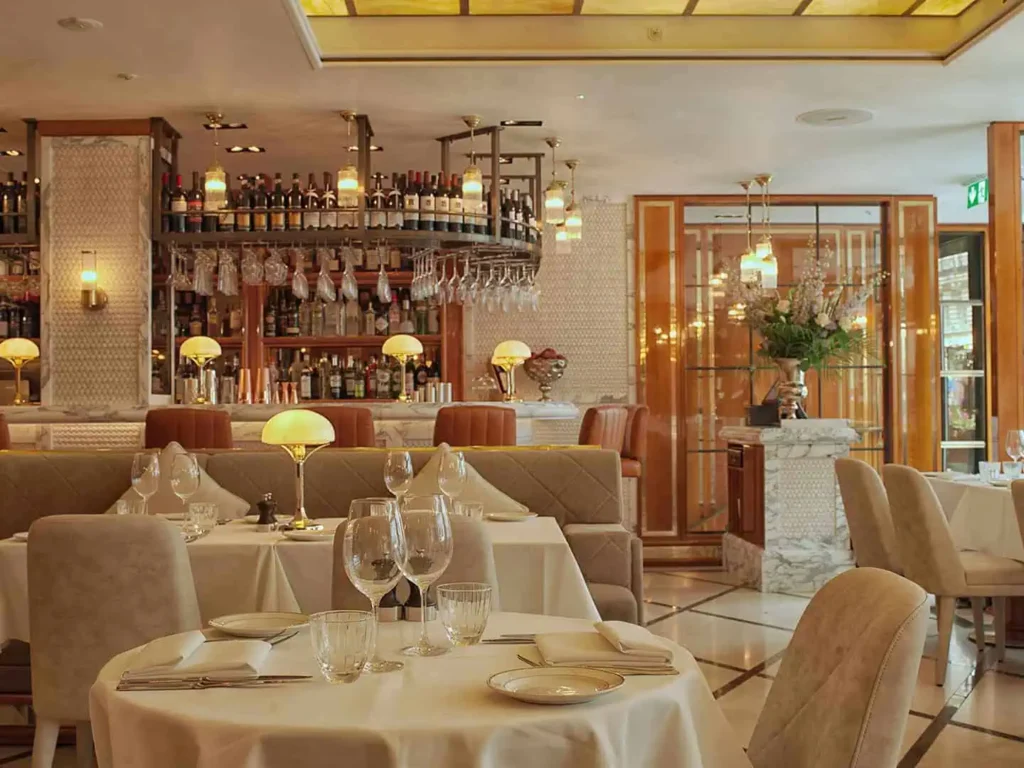 Elegant restaurant interior with stylish tables, ambient lighting, and a well-stocked bar in the background.