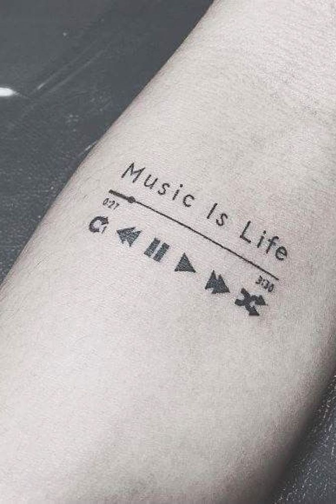 Tattoo on forearm featuring music player controls and Music Is Life text, symbolizing love for music.