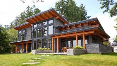 Modern wooden house exterior with large windows, surrounded by lush greenery and trees.