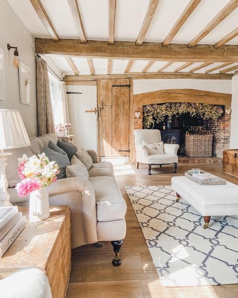 Cozy rustic living room with wooden beams, fireplace, comfy sofas, and floral accents for a warm farmhouse style.