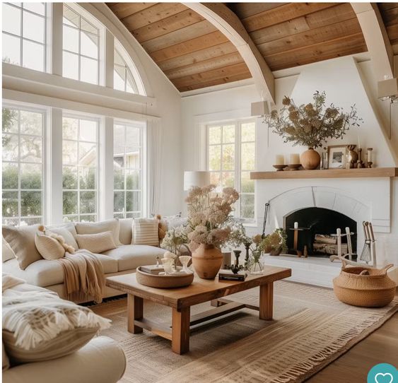 Cozy living room with rustic decor, vaulted ceiling, wooden beams, and a large window bringing in natural light.