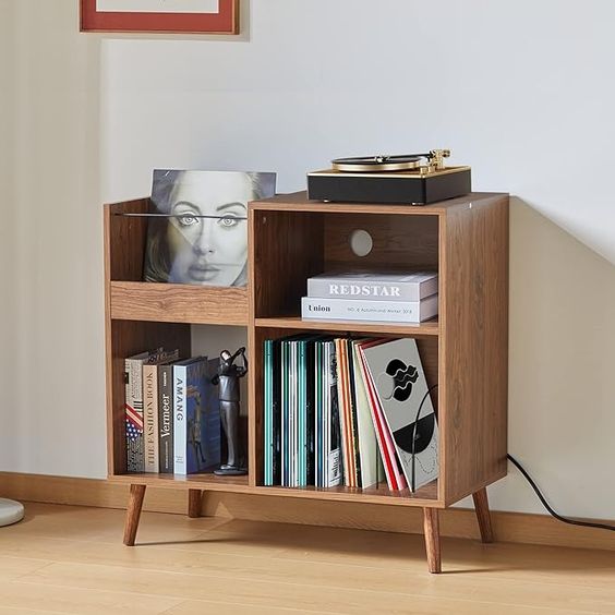 Mid-century modern vinyl record player stand with LP records, books, and a framed picture on a wooden floor.